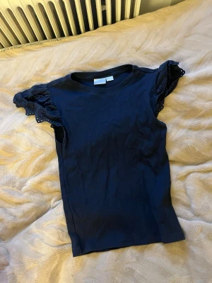 Blå topp med volangärmar - Säljer en blå topp med korta volangärmar i broderad bomull. Toppen har rund hals och är figurnära i modellen. Perfekt för dig som gillar detaljer och vill ha något enkelt men ändå med en twist.