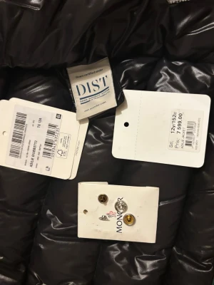 Mörkgrön Moncler dunjacka 12 år - Säljer en mörkgrön dunjacka från Moncler med klassisk logga på ärmen och coolt serietidningsfoder på insidan. Jackan är quiltad och har en glansig finish som ger en lyxig vibe. Perfekt för dig som vill ha något både snyggt och varmt.