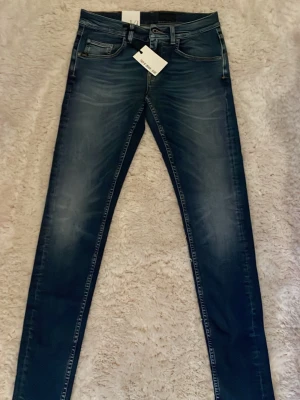 Tiger of Sweden blå jeans W29 L34 - Snygga blå jeans från Tiger of sweden. Jeansen har klassisk femficksdesign, bruna detaljer vid bakfickan och är tillverkade i jeansmaterial. Perfekt för dig som gillar en modern och stilren look. Nypris: 1600kr
