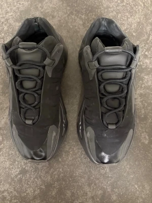 Adidas Yeezy 700 V3 sneakers svart/grå - Säljer ett par Adidas Yeezy 700 V3 sneakers i svart och grått med chunky sula och reflekterande detaljer på sidan. Skorna har snörning och en rund tå, tillverkade i syntet och mesh för en cool och modern look. Perfekt för dig som gillar streetwear och unika sneakers.