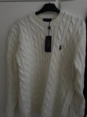 Vit kabelstickad tröja Polo Ralph Lauren - Säljer en vit kabelstickad tröja från Polo Ralph Lauren med klassisk rund hals och broderad logga på bröstet. 