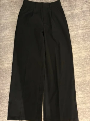Svarta wide kostymbyxor - Snygga svarta kostymbyxor med wide fit och klassisk midja. Byxorna har raka ben och diskreta fickor framtill.  Byxorna är lite noppiga baktil, går att ta bort. 