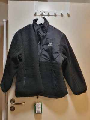 Svart  jacka från New Balance - Svart jacka från New Balance. Man kan ha den båda in och ut så det kan bli en teddyjacka men också en dunjacka. Varm och skön. Helt ny