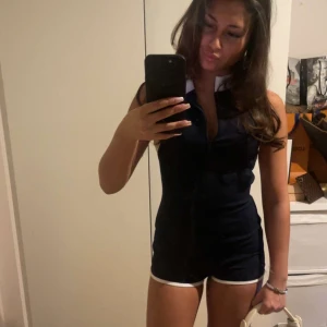 Mörkblå byxdress med vit krage - Säljer en sportig mörkblå byxdress med vit krage och vita detaljer längs bensluten. Byxdressen är ärmlös, har dragkedja framtill och är kort i modellen. Perfekt för dig som gillar en stilren och fräsch look. Justerbar storlek S men funkar XS också💕 helt ny med prislapp (ordpris 299)