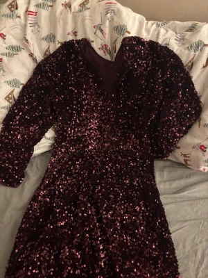 Vinröd paljettklänning med puffärm - Säljer en vinröd kortklänning med glittriga paljetter över hela klänningen. Klänningen har långärmade puffärmar och en snygg v-ringad rygg. Perfekt för dig som vill sticka ut med en glammig look. Materialet är polyester och klänningen har en figurnära passform. Klänningen är nyligen inköpt och aldrig använd, har tyvärr inte kvar lappen men den är köpt på HM. Perfekt för det kommande nyåret t.ex.