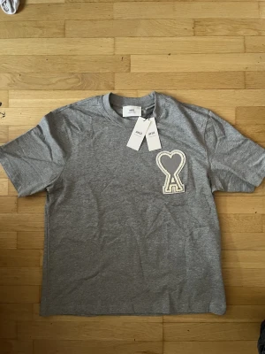 Grå t-shirt från Ami med hjärtdetalj - Snygg grå t-shirt från Ami Alexandre Mattiussi med ett stort broderat hjärta och bokstaven A på bröstet.