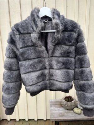 Grå pälsjacka i storlek 34 - Säljer en fluffig och riktigt snygg grå pälsjacka med horisontella paneler. Jackan har hög krage, långa ärmar och ribbade muddar vid ärmslut och nederkant. Perfekt för dig som vill ha en statementjacka i vinter. 