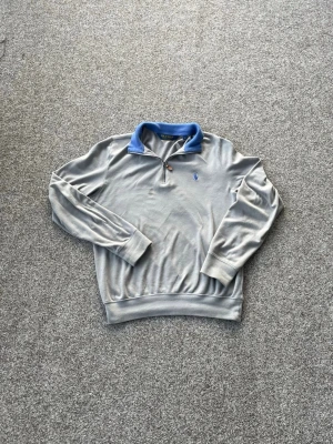 Grå half zip tröja från Ralph Lauren - Säljer en grå långärmad tröja från Polo Golf Ralph Lauren med blå krage och broderad blå logga på bröstet. Tröjan har half zip-dragkedja och är tillverkad i mjuk bomull, perfekt för chill höst- och vårdagar.Kom gärna med prisförslag och frågor😃