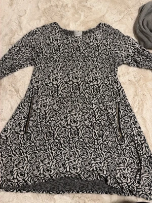 Svartvit blommig klänning Masai - Säljer en svartvit klänning från Masai med lång ärm och blommigt mönster. Klänningen har rund halsringning och två dekorativa dragkedjor framtill. Materialet är mjukt och känns som bomull. Perfekt för dig som gillar unika prints och bekväm stil.