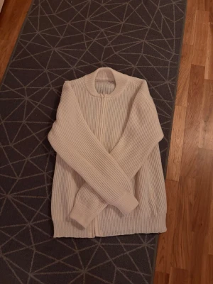 Beige ribbad kofta med dragkedja - Säljer en beige ribbstickad kofta med dragkedja framtill. Koftan har långärmad design, rundad hals och är gjord i ett mjukt stickat material. Perfekt för lager-på-lager och chill dagar.