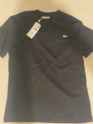 Svart Lacoste t-shirt classic fit - Svart t-shirt från Lacoste i classic fit för män med den ikoniska krokodilloggan och broderad Lacoste-text på bröstet. Aldrig använd med prislappen kvar och köpt från Zalando för 849kr.