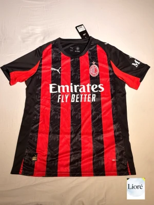 AC Milan matchtröja Puma röd/svart - Säljer en officiell AC Milan matchtröja från Puma med klassiska röda och svarta vertikala ränder. Tröjan har klubbmärke på bröstet, Puma-logga och sponsortryck framtill. Tillverkad i lätt polyester med rund hals och korta ärmar.