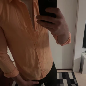 Persikofärgad skjorta Tiger of Sweden - Säljer en persikofärgad skjorta från Tiger of Sweden. Skjortan har klassisk krage, långa ärmar och knappar framtill. Tillverkad i mjuk bomull och har en clean, stilren look som passar perfekt till jeans eller chinos.