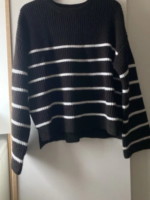 Svartvit randig stickad tröja Kappahl - Mysig svart stickad tröja från Kappahl med vita horisontella ränder. Tröjan har en relaxed fit, ribbade muddar och rund hals. Perfekt för kyliga dagar och enkel att styla med jeans eller kjol.