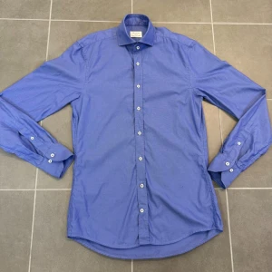 Blå skjorta från Stenströms - Säljer en blå slimline skjorta från Stenströms i twofold super cotton. Skjortan har klassisk krage, vita knappar och lång ärm. Perfekt för dig som gillar stilrena och tidlösa plagg.