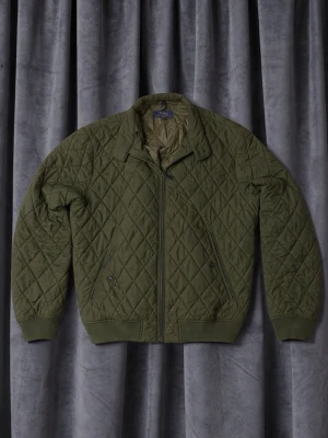 Ralph Lauren jacka  - Säljer en olivgrön quiltad jacka från Polo Ralph Lauren. Jackan har dragkedja framtill, ribbade muddar och två fickor med knappstängning. Klassisk bombermodell med rutmönster och mjukt foder, perfekt för kyligare dagar.