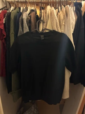 Svart topp från Lindex, storlek S - En enkel svart topp från Lindex i storlek S. Modellen har rund halsringning med ribbad kant och korta ärmar. Perfekt basplagg som funkar till allt och är lätt att matcha. Materialet känns mjukt och bekvämt.