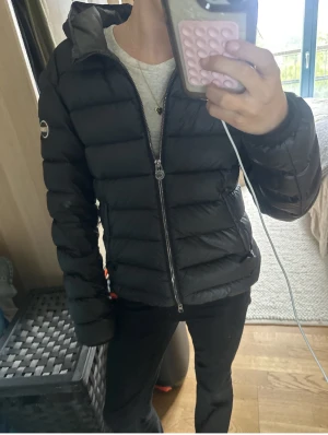 Colmar vinter/vår  jacka  - Snygg svart dunjacka från Colmar med dragkedja och huva. Jackan har en quiltad design och en rund logotyp på ärmen. Passar xs/s