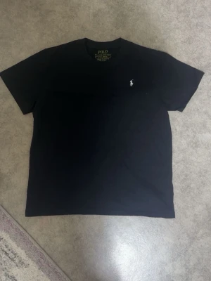 Svart t-shirt från Polo Ralph Lauren - Klassisk svart t-shirt från Polo Ralph Lauren med slim fit passform. T-shirten har rund halsringning och den ikoniska broderade loggan i vitt på bröstet. Tillverkad i mjuk bomull som känns skön mot huden.