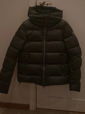 Svart pufferjacka från Colmar - Säljer en grön pufferjacka från Colmar Originals med huva och dragkedja framtill. Jackan har en clean look med diskret logga på ärmen och breda, quiltade partier. Perfekt för kalla dagar och riktigt snygg till streetwear-stilen.