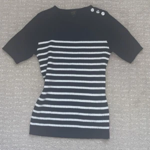 Randig kort ärmad tröja - Superfin topp i svart och vitt med ribbad struktur och klassisk randig design. Figurnära passform och fina knappdetaljer på axeln som ger det lilla extra. Passar både till en fin sommar outfit men också vinter,höst.