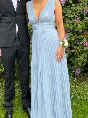 Ljusblå plisserad långklänning - Säljer min superfina balklänning som jag älskade, den är från asos och är i storlek 38. Den är ljus blå  och plisserad i tyget, den har även ett band i midjan som man kan knyta hur man vill men jag valde att knyta en rosett i ryggen.