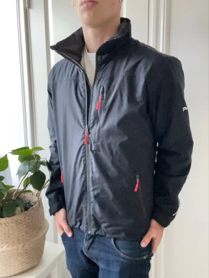 Helly Hansen regnjacka  - Helly Hansen regnjacka / vindjacka. Den klassiska helly Hansen regnjacka / vindjacka. Med HH loggan omkring jackan och plast fickan på ryggen. Inga defekter på jackan - en väldigt trevlig jacka som passar perfekt för vintern och våren. Otroligt najs passform på modellen som är 180 cm 75 kg! Den är igentligen mer blå det är bara konstigt ljus 