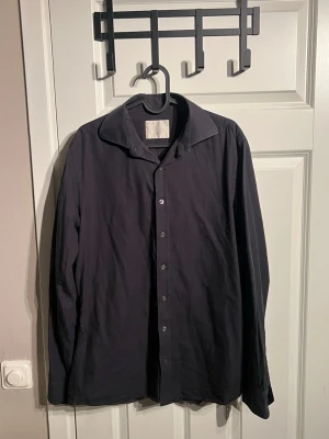 Svart skjorta från Oscar Jacobson - Klassisk svart skjorta från Oscar Jacobson med lång ärm och knappar framtill. Skjortan har en stilren, tidlös design och är tillverkad i mjuk bomull som känns skön mot huden. Mer frågor eller bilder är det bara att fråga! Storlek 40= m