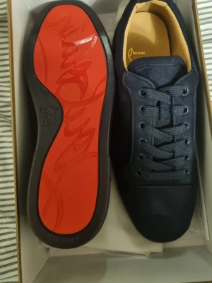 Marin blå  sneakers från Christian Louboutin - Säljer ett par svarta sneakers från Christian Louboutin i mocka med den ikoniska röda sulan. Skorna har rund tå, snörning och diskret broderad logga på hälen. Insidan är beige och de kommer i originalkartong med dustbag.