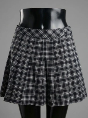 Svartvit rutig kortkjol med knapp - Säljer en svartvit rutig kortkjol med klassiskt veckad design och en silverfärgad knapp i midjan. Kjolen har en A-linjeformad siluett och är gjord i ett mjukt, vävt material som känns bekvämt. Perfekt för dig som gillar preppy stil och vill ha något som sticker ut.