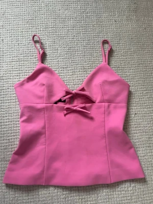 Rosa korsettopp med rosetter från Zara - Supersöt rosa korsettopp från Zara med smala axelband och två dekorativa rosetter framtill. Toppen har en snygg v-ringning och dragkedja i ryggen för enkel påklädning. Materialet känns mjukt och följsamt, perfekt för att lyfta vilken outfit som helst. Den är helt slutsåld och väldigt eftertraktad! 