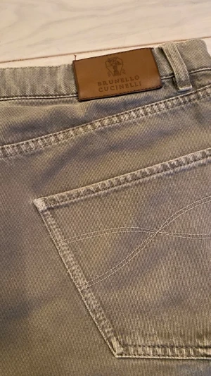 Gråa jeans från Brunello Cucinelli - Säljer ett par gråa jeans från Brunello Cucinelli med slitna detaljer på framsidan. Byxorna har klassisk femficksdesign, normal passform och är tillverkade i bomull. Snygg läderpatch med loggan bak vid midjan. Nypris runt 5000kr. Hör av dig vid intresse!