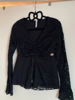 Svart spetsblus med snörning - Säljer en svart blus från chiara forthi  med långa ärmar i spets och v-ringning. Toppen har snygg snörning framtill och lätt utsvängda ärmslut. Materialet är genombruten spets som ger en cool look❤️❤️Det är storlek s men jag skulle säga att den är mer som xs 