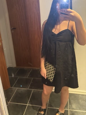 Svart kort klänning från H&M Divided - Svart kort klänning från H&M Divided i storlek 38. Klänningen har tunna axelband, lätt rynkning vid bysten och en luftig passform. Perfekt till sommaren och enkel att styla med olika accessoarer.