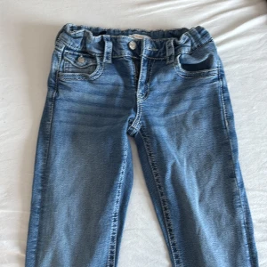Blå bootcut jeans Gina Tricot 164 - Säljer ett par blå bootcut jeans från Gina Tricot i storlek 164. Jeansen har snygga broderade bakfickor med knappdetaljer och klassisk femficksdesign. Tillverkade i mjukt denimtyg med normal passform och utsvängda ben.
