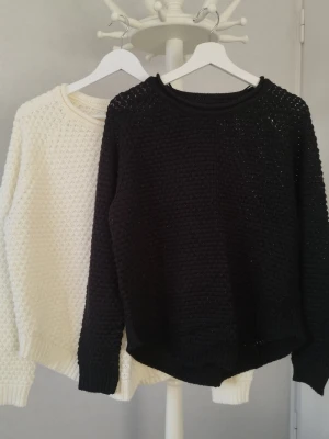 Vit stickad tröja från Vero Moda - Säljer en vit och en svart stickad tröja från Vero Moda i storlek L. Tröjorna har ett snyggt strukturmönster, rund halsringning och ribbade muddar vid ärmslut och nederkant. Perfekt för lager på lager under höst och vinter. Se de sista två bilderna. Finns lite trådragningar och noppror på. Men annars i fint skick.