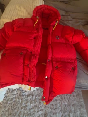 Röd Expedition down lite jacket  - Säljer en röd Fjällräven jacka i Expedition down lite storlek XXS. Kemtvättad för 400kr.  Liten fläck på ena knappen och ena snöret inuti är också lite trasigt.