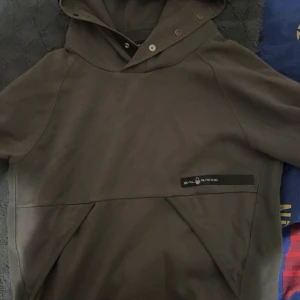 Sail racing hoodie - En sailracing hoodie i färgen grå med en stor ficka och som man kan knäppa vid luvan. Perfekt under vintern men även för sena sommarkvällar