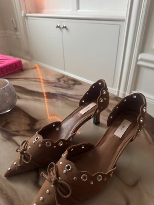 Bruna klackskor med detaljer från Nelly - Snygga bruna klackar från Nelly i mockaimitation med spetsig tå, låg klack och coola silverfärgade detaljer. Skorna har vågig kant och en söt rosett framtill som ger en unik touch. Perfekta för dig som vill sticka ut med detaljer och stil!!!!❤️❤️ skorna är oanvända då dom är fel storlek!