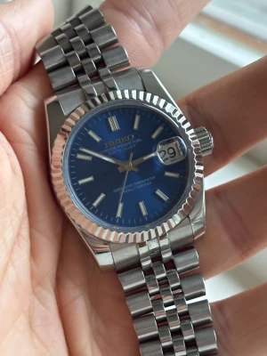 Seiko Datejust blå urtavla stål - Säljer en snygg Seiko Mod Datejust med blå urtavla och silvrigt stålarmband. Klockan har en räfflad bezel, datumfönster med förstoring och automatiskt urverk som syns genom bakboetten. Klassisk och stilren design med markerade index och robust länkarmband. NH35 urverk. Får med låda och extra länkar! 36mm, passar därmed nästan alla!