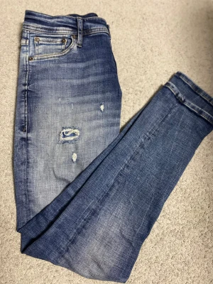 Blå jeans från Jack & Jones - Snygga blå jeans från Jack & Jones med slitningar och lagad detalj på låret. Klassisk femficksmodell med ljus tvätt och kontrastsömmar. Jeansen har rak passform och är tillverkade i mjukt denimtyg för en bekväm känsla.