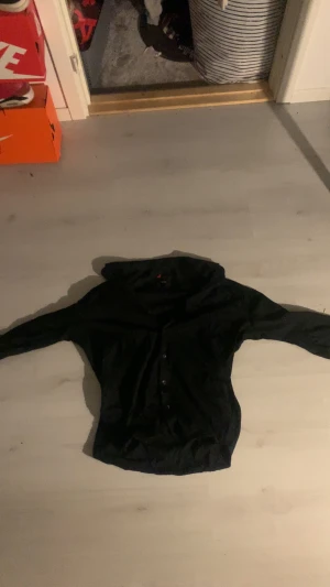 Svart slim fit skjorta Dressmann XL - Svart skjorta från Dressmann i slim fit-modell, storlek XL (43/44). Klassisk design med knappar framtill och lång ärm. Skjortan är stilren och passar dig som gillar en smalare passform. Materialet är mjukt och bekvämt, perfekt för dig som vill ha en enkel och snygg look.