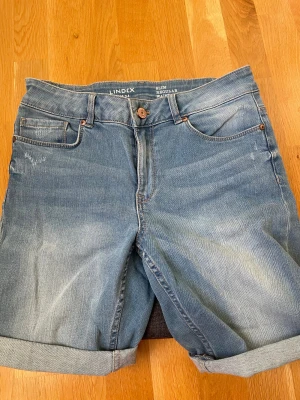 Blå jeansshorts från Lindex - Snygga blå jeansshorts från Lindex med uppvikta benslut. Shortsen är mid waist och har några slitna detaljer.