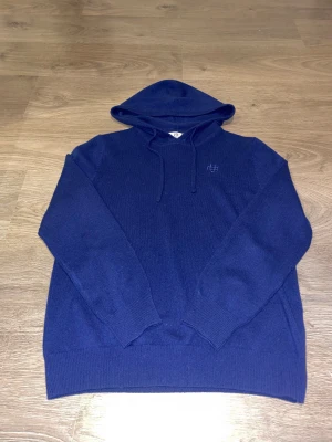 Marinblå hoodie från Bvaldi storlek S - Snygg marinblå hoodie från Bvaldi med broderad logga på bröstet. Tröjan har huva med snörning och är tillverkad i mjuk stickad ull. Långärmad modell med ribbade muddar vid ärmslut och nederkant. Perfekt för dig som gillar stilren och enkel design. Aldrig använd då den var för liten för mig 