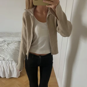 Beige stickad kofta - Säljer en beige stickad cardigan jacka med dragkedja framtill. Jackan har en loose passform, ribbad struktur och lång ärm. 