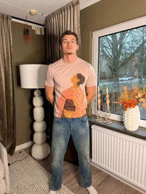 Beige t-shirt med konsttryck från Elvine - Snygg beige t-shirt från Elvine med ett stort konstnärligt tryck framtill som föreställer en person i rutig skjorta. T-shirten har rund hals och korta ärmar, och är gjord i mjuk bomull som känns skön mot huden. Perfekt för dig som gillar unika prints.