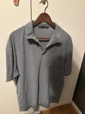 Grå frottéskjorta  - Grå skjorta i mjuk frotté från 157, med klassisk krage, kort ärm och bröstficka. Perfekt för dig som gillar chill och avslappnad stil. Enkel och stilren design som funkar året runt. 30kr och den är din. 