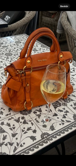 Orange handväska från Miu Miu i skinn - Säljer nu min orangea miumiu bow-bag (äkta) Orangefärgad handväska med dubbla handtag och guldfärgade detaljer. Säljer den för att jag känner att den har gjort sitt och att det är dags för någon annan att älska den 🧡 (köpt på Vestiaire Collective i maj) för mer bilder på väskan kan man bara skriva till mig så löser jag det såfort som möjligt. Är man intresserad men känner att väskan inte är värd pengen, skriv så kommer vi överens om annat