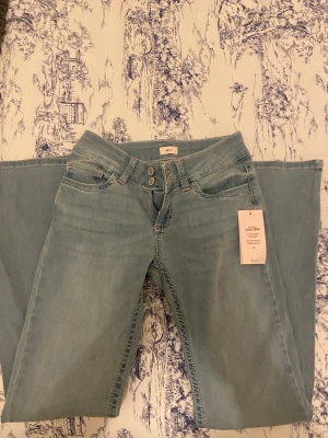 Ljusblå bootcut jeans från Nelly - Säljer ett par ljusblå jeans från Nelly med bootcut-modell. Jeansen har låg midja, två knappar framtill och en snygg detalj med rosa broderi på bakfickan. Tillverkade i mjukt denimtyg✨