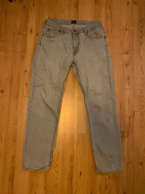 Lee ljusblå jeans W32 L32 - Säljer ett par klassiska ljusblå jeans från Lee i rak modell. Jeansen har fem fickor, Lee-logga på knapp och bak, samt slitna detaljer vid benslut. Tillverkade i bomull för skön känsla och snygg passform. Perfekt för dig som gillar vintage-vibe. Är även lite slitna vid rumpan men det märks knappt. Priset är inte hugget i sten.